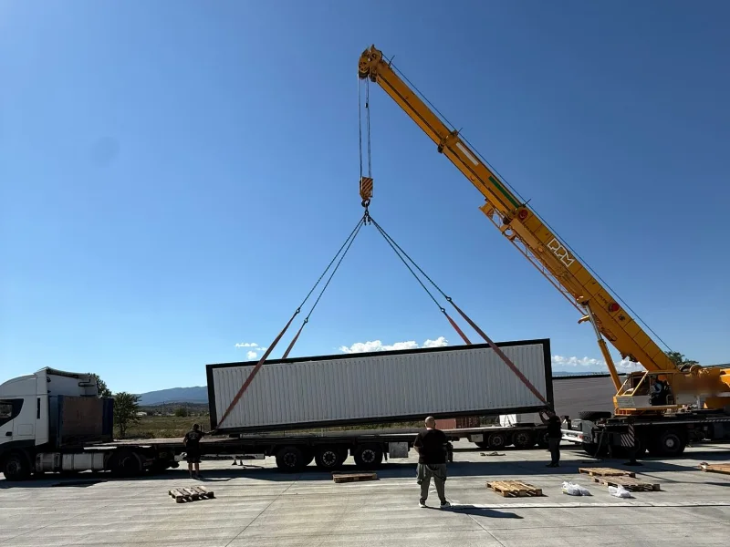 A crane lifting a long module off a truck onto a concrete yard