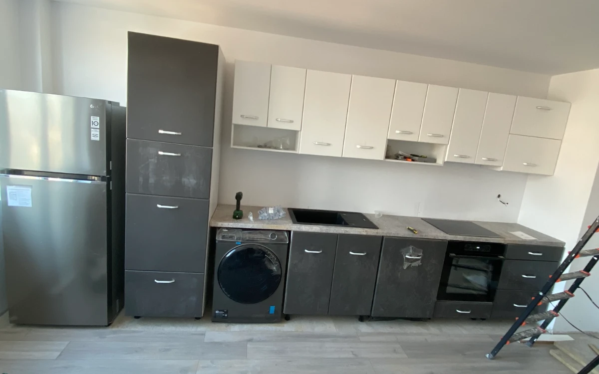 The apartment kitchen after the cabinets were fitted: fridge, tall unit, white wall cabinets and dark base units with washing machine and oven